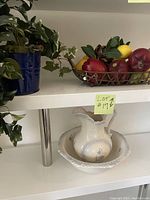 Shelf display showing faux plant in blue metal bucket, metal basket with faux fruit, and ceramic jug and pitcher set in wash basin.