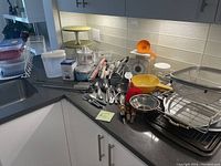 Full view of kitchen corner counter with various kitchen utensils including spoons, ladles, vintage scale, plastic containers, small electric juicer, and other items.