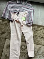 Full view of the light pink slacks laid out with the variegated shawl on top, showing size and general condition.