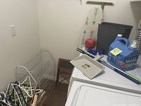 View of laundry items including ironing board, fabric softener container, dustpan, broom, step stool, and wire shoe rack in corner of room