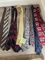 All nine men's ties laid flat on wooden floor showing various patterns and colors including floral, paisley, stripes, and Christmas-themed novelty prints.