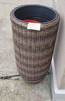 Tall bamboo style planter pot shown from side view leaning against building exterior wall.