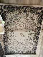 Floral pattern linen area rug with cream center and dark floral border shown flat on floor.