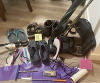 Photo showing a variety of shoes including sandals, slip-ons, flip-flops, and hiking boots, along with fishing rods, walking poles, and personal care items on the floor.