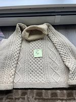 Full front view of cream-colored vintage hand knit sweater showing intricate Aran style cable and diamond patterns with cowl neck.