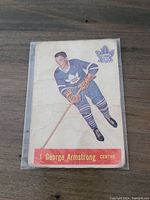 Front of 1957-58 George Armstrong Parkhurst hockey card showing player in blue Toronto Maple Leafs uniform with creases and wear.
