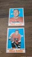 Front view of two 1970 O-Pee-Chee Flyers hockey cards, Larry Hillman and Joe Watson, showing player portraits and team info.