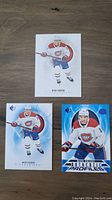 Three Nick Suzuki hockey cards on wooden background. One card shows Suzuki skating forward, one is a profiles card with blue background, last one shows Suzuki in Canadiens white jersey.