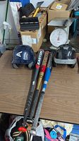 Overview of the three baseball bats laid flat on a table with two helmets on either side. The bats display branding and colors: Easton (black), Worth (gold/red), Big Stick (blue/white). Helmets are navy blue and black/white.