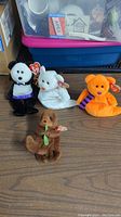 Four Beanie Babies plush toys including a panda, tiger cub, orange bear, and brown dog on a table