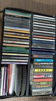 Two stacks of mixed CDs, cassette tapes, and DVDs showing the varied titles and condition.