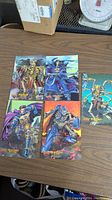 Top-down photo of 5 Darkstalkers comic prints on a wood table showing various characters including skeleton warriors and armored figures.