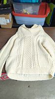 Front view of the cream-colored hand knit Irish sweater laid flat, showing cable and honeycomb pattern and ribbed hem.
