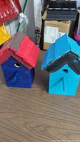 Two handmade painted wooden birdhouses on a table, showing front angles with visible entrance holes and perches.