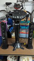 Front view of karaoke machine console standing on pedestal with two black tower speakers on each side on a table surface.