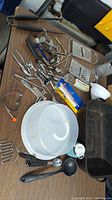Photo of assorted kitchen tools including graters, corkscrews, measuring spoons, ladle, ice crusher, and other bar and cooking tools on a brown table.