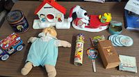Full view of the lot showing Cabbage Patch doll, Snoopy sled music box with doghouse base, tin can, toy train, kaleidoscope, clown paddle, box, and coasters.