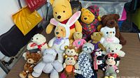 Photo showing the full lot of 16 assorted stuffed animals on a table including Winnie the Pooh, Minnie Mouse, various teddy bears and other plush characters
