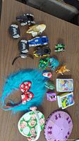 Various small toys arranged on table including multi-part Transformers vehicle pieces, small character figures (Power Rangers, animals), blue fuzzy headband with dice, rotating toy with animal figurines, and small card decks.