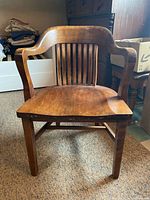 Front view of wooden bankers style desk armchair showing curved backrest with vertical slats and curved armrests.
