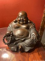 Front angle showing full seated Buddha with smiling expression, bead necklace in right hand, detailed robe texture.