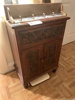 Front angled view showing entire hardwood cabinet with carved floral designs, drawer, double doors, and rounded knobs.