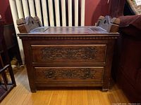 Front view of wood carved chest showing floral details on two front panels and solid square legs.