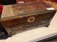 Angled front view showing decorative carvings on front panel, latch hardware and glass top