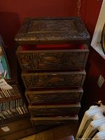 Chest of drawers with all drawers opened illustrating interior lined with red felt and carved wooden exterior.