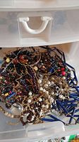 Tangled plastic drawer compartment showing assorted bead and chain necklaces in various colors and materials