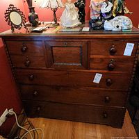 Front view of antique wood dresser showing multiple drawers and decorative central panel with turned wood knobs