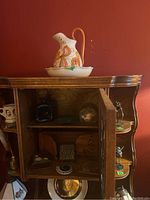 Glass decanter with stopper, carved wooden panels, and various small figurines inside wooden cabinet with open door.