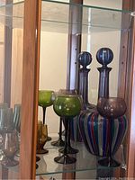 Assorted colored glasses and striped decanter displayed inside a glass cabinet