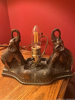Front view of vintage elephant lamp base with clear filament bulb and raised elephants on base.