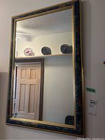 Front view of a rectangular wall mirror showing its full painted and gilded frame with beveled glass reflecting a room interior.