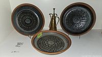 Front view of three stoneware plates with terracotta rims and black radial glaze patterns, with brass-tone oil dispenser behind