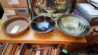 Three pottery bowls on wooden table, the largest signed Reddick, showing different glaze styles and sizes