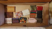 Photo showing assortment of small purses and coin pouches laid flat in drawer, variety includes leather and fabric materials, mix of colors and patterns.