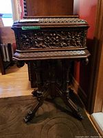 Front view of carved sewing box on stand showing overall form and carving pattern