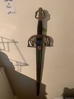 Full view of decorative Spanish blunted sword leaning against wall, showing entire length and ornate metal guard.