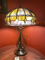Full view of the table lamp showing the metal base and stained glass shade lit against a red wall.