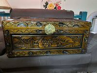 Front view of the carved wood chest showing detailed scenes and decorative edges with a brass latch.