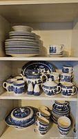 Photo showing teapot, salt shakers, creamer, mugs, cups and saucers, and a serving platter on a middle cabinet shelf.