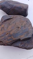 Close view of two dark brown-black banded iron stones with rusty orange streaks on white background