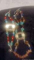 Photo showing two handmade stone and glass bead bracelets with silver-tone square centerpiece beads, one mainly blue and red, the other brown and turquoise toned.