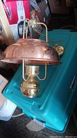 Copper hanging light fixture resting on a teal storage bin, showing the dome-shaped copper shade and brass base.