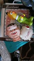 Photo showing Burt piggy bank in green outfit, Hardy puppet doll, and needlepoint kit with stamp.