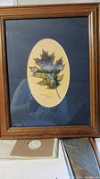 Full view of framed artwork showing the wooden frame, oval mat, and painted maple leaf with elk scene.
