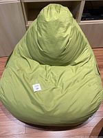 Front view of the green bean bag chair showing its overall shape and fabric texture with minor stains.