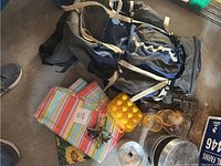 View of Kelly Redcloud 5600 backpack with camping supplies arranged around it including pots, cups, tablecloths, yellow egg carton and tent pegs.